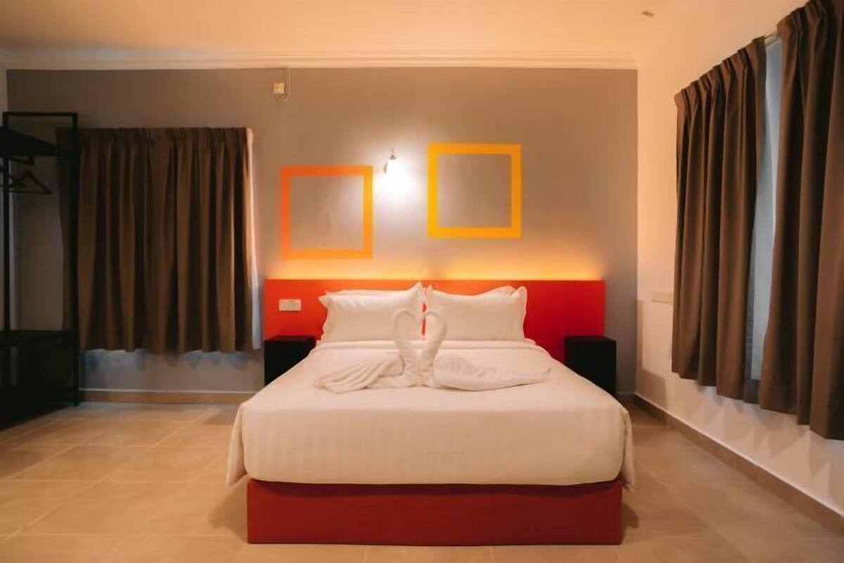 Una habitación de hotel con una cama, dos mesitas de noche, una pared de acento roja y cortinas.