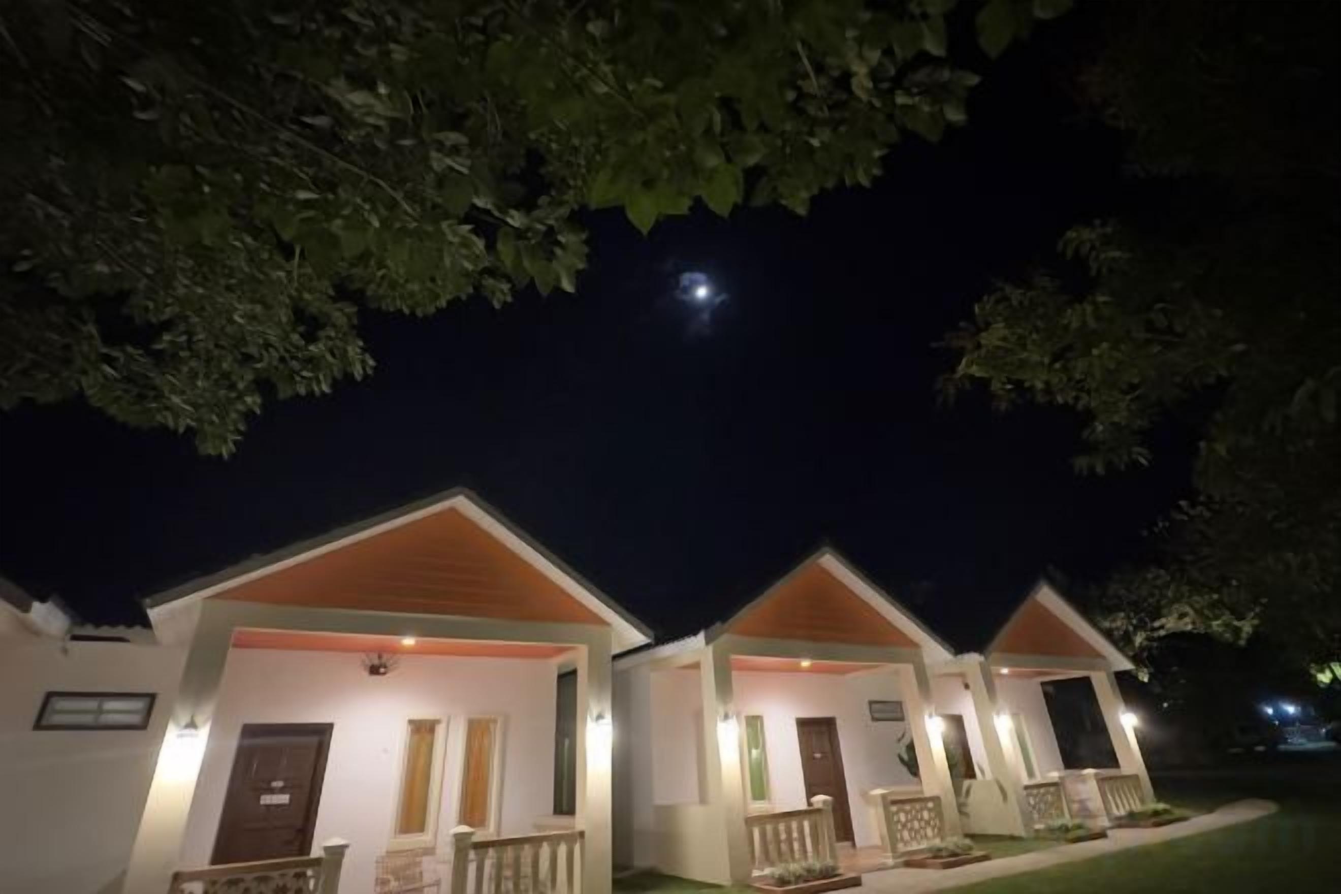 Una hilera de cabañas de un piso con porches delanteros, bajo un cielo nocturno con una luna visible.