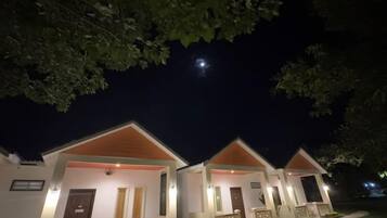 Una hilera de cabañas de un piso con porches delanteros, bajo un cielo nocturno con una luna visible.