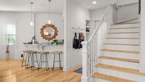 Eine moderne Küche mit einer Sitzecke an einer Holzbar, einem großen Spiegel und einer Treppe mit weißen Geländern.