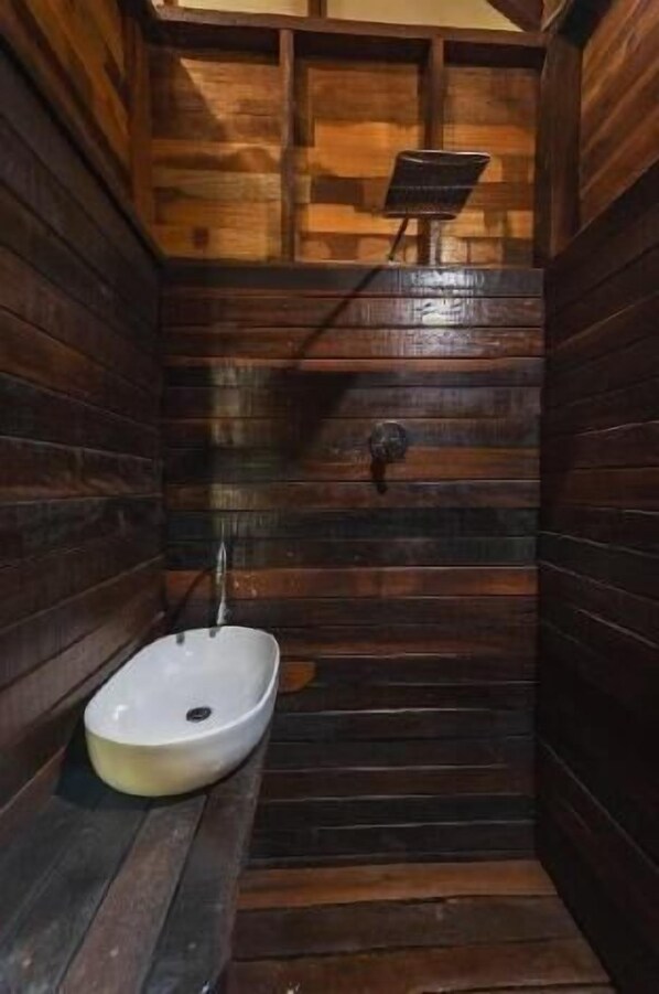 Une salle de bain de style rustique, avec des murs en bois, un lavabo blanc et une douche.