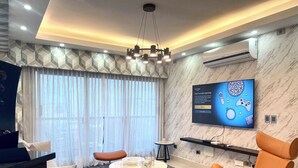 A modern living room with a marble wall, a flat-screen TV, a dining area with a round table, and a sofa.
