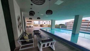 A modern indoor pool area with a seating area, a view of the pool, and a building in the background.