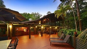 An outdoor deck with wooden flooring, lounge chairs, and a covered seating area with tables and chairs. - Wait-a-While Eco Retreat (Cow Bay)