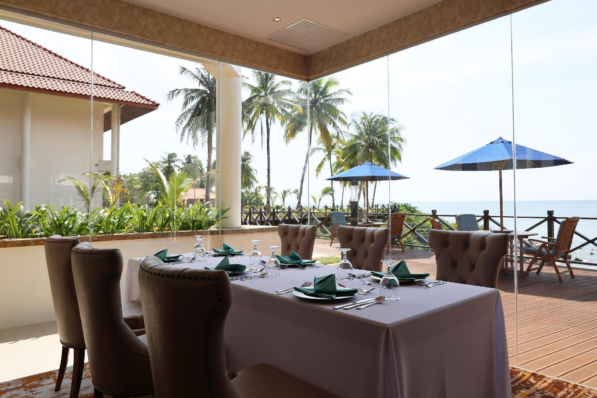A dining area with a view of the ocean, furnished with tables and chairs, and equipped with umbrellas.