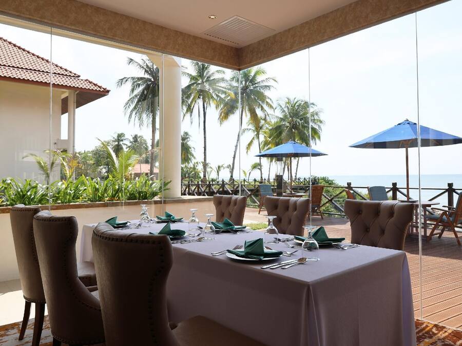 A dining area with a view of the ocean, furnished with tables and chairs, and equipped with umbrellas.