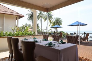 A dining area with a view of the ocean, furnished with tables and chairs, and equipped with umbrellas. - Damai Lagoon Resort (Kuching)