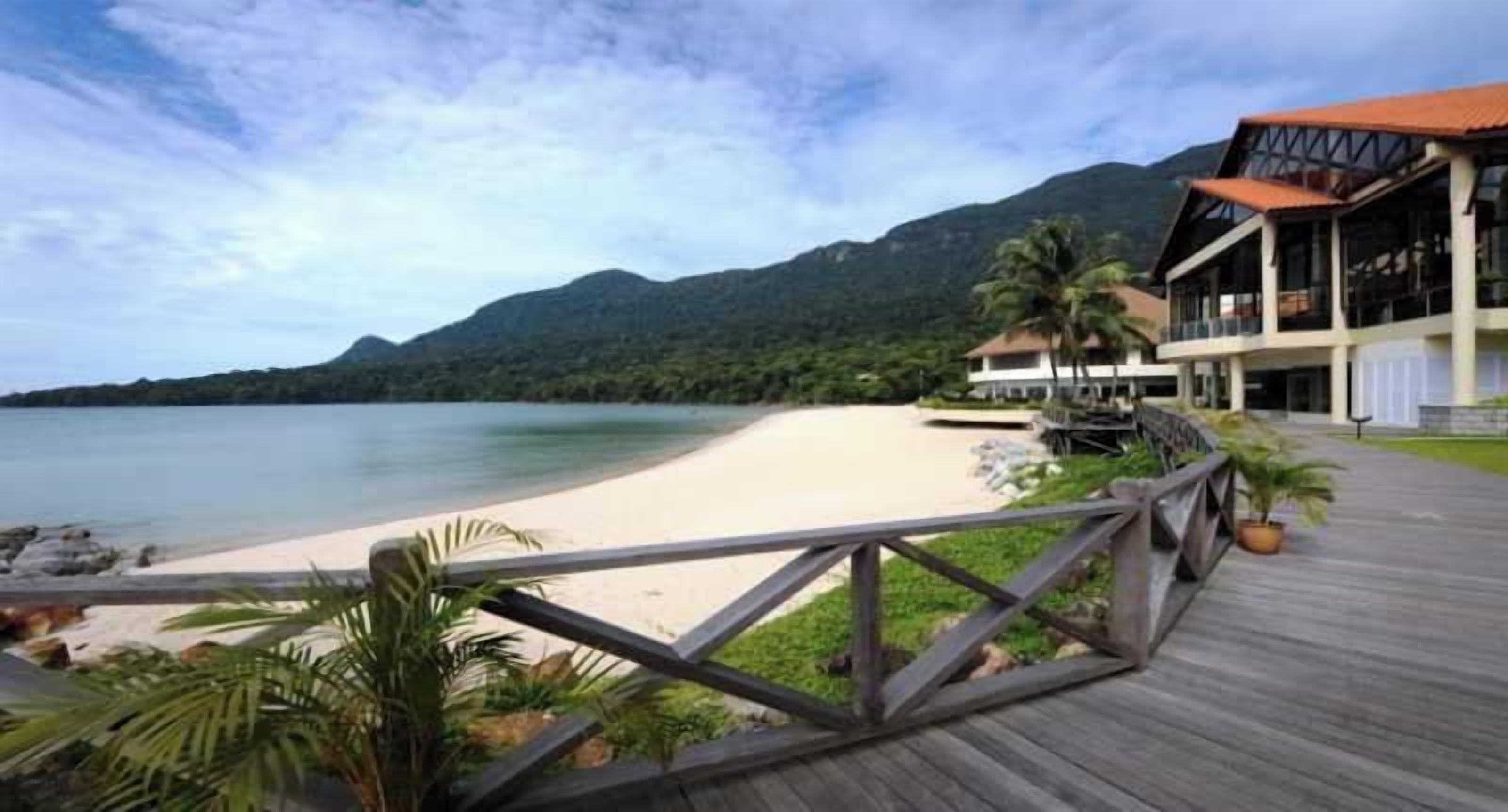 A beach resort with a wooden boardwalk, a sandy beach, and a mountain backdrop.