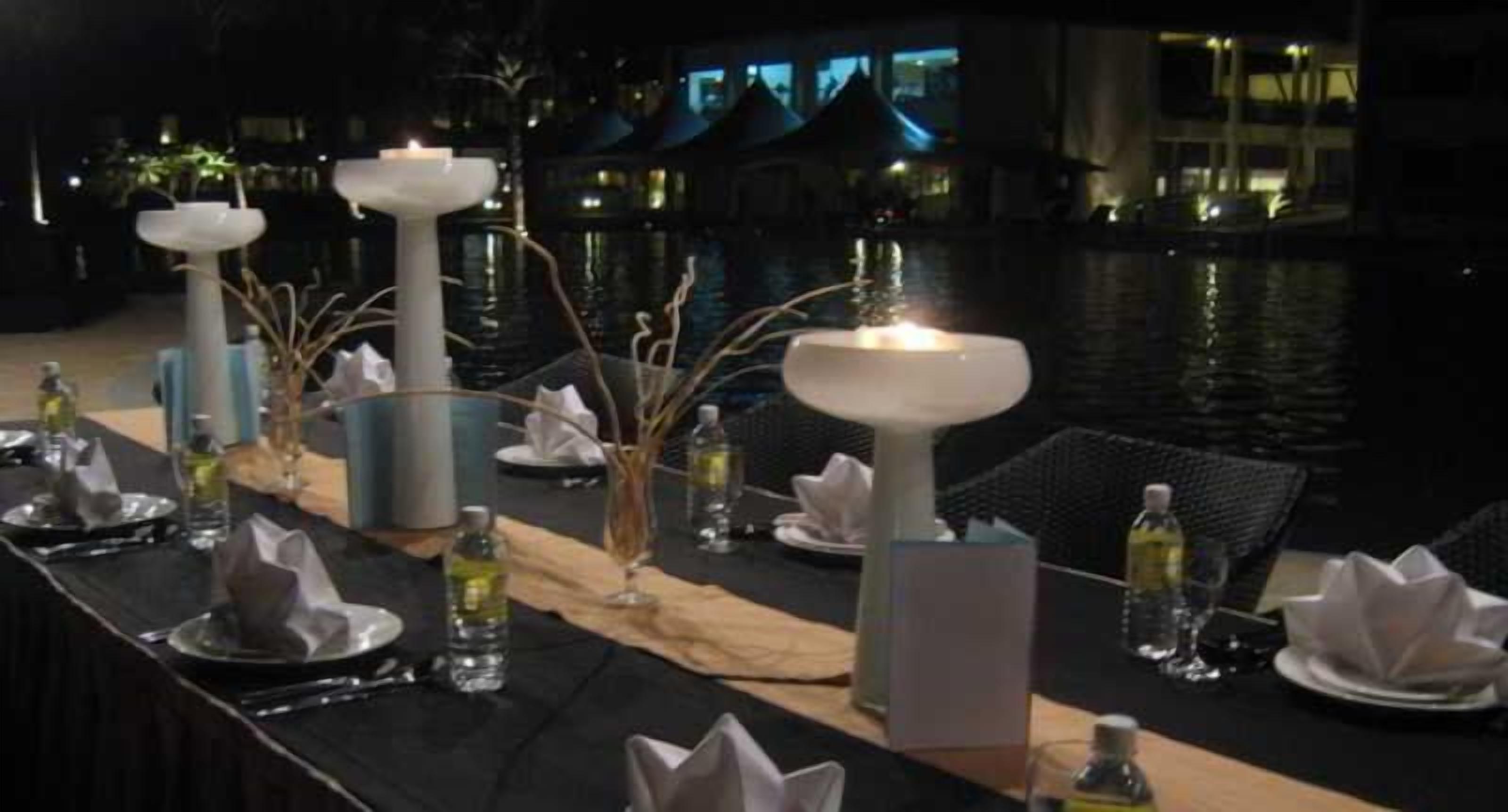 A dining table set with candles, plates, and glasses, overlooking a body of water.