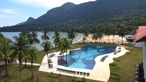 Un resort con piscina, spiaggia, palme e montagne sullo sfondo.
