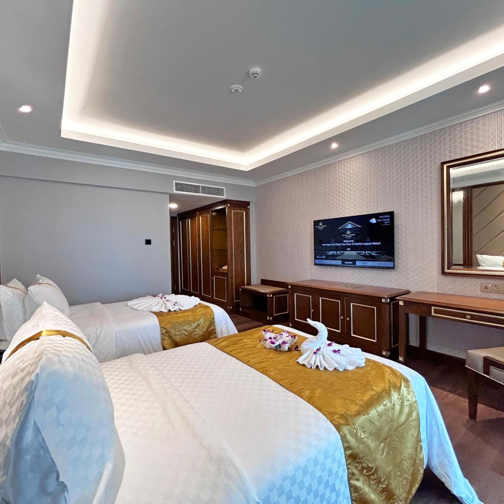 A hotel room with two beds, a TV, a desk, and a mirror.