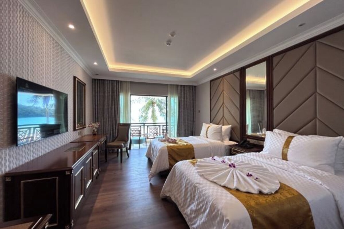 A hotel room with two beds, a TV, a desk, and a balcony with a view.