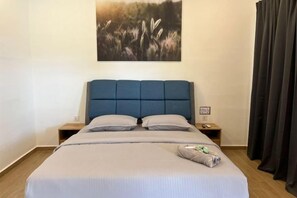 A neatly made bed with a blue headboard, a bedside table with a lamp, and a painting of a field on the wall. - Raintown Cottage (Tupai)