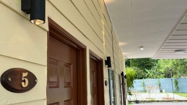 A building facade with a number '5' sign, a wooden door, and a covered walkway with a view of greenery. - Raintown Cottage (Tupai)