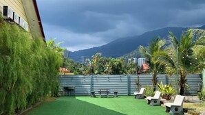 A courtyard with artificial grass, outdoor seating, and a view of mountains. - Raintown Cottage (Tupai)