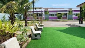 A well-maintained lawn with outdoor seating and a row of colorful buildings in the background. - Raintown Cottage (Tupai)