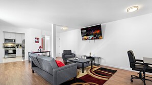 Una sala moderna con un sofá gris, una silla de oficina negra, una mesa de centro y un televisor en la pared mostrando 'Stranger Things'.
