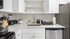 Una cocina moderna con armarios blancos, un lavamanos de acero inoxidable, lavavajillas y varios electrodomésticos.