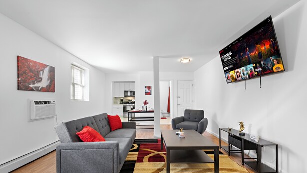 Una sala de estar moderna con un sofá gris, cojines rojos, una mesa de centro y un televisor que muestra 'Stranger Things'.