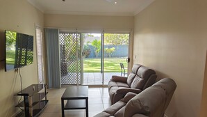 Ein Wohnzimmer mit einer Couch, einem Fernseher und einer Glasschiebetür, die in einen Garten führt.