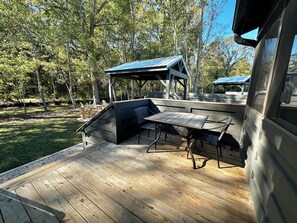 Une terrasse en bois avec une table et des chaises intégrées, entourée d’arbres.