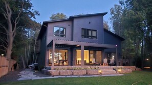 A modern two-story house with a covered patio, stone steps, and a well-maintained lawn.