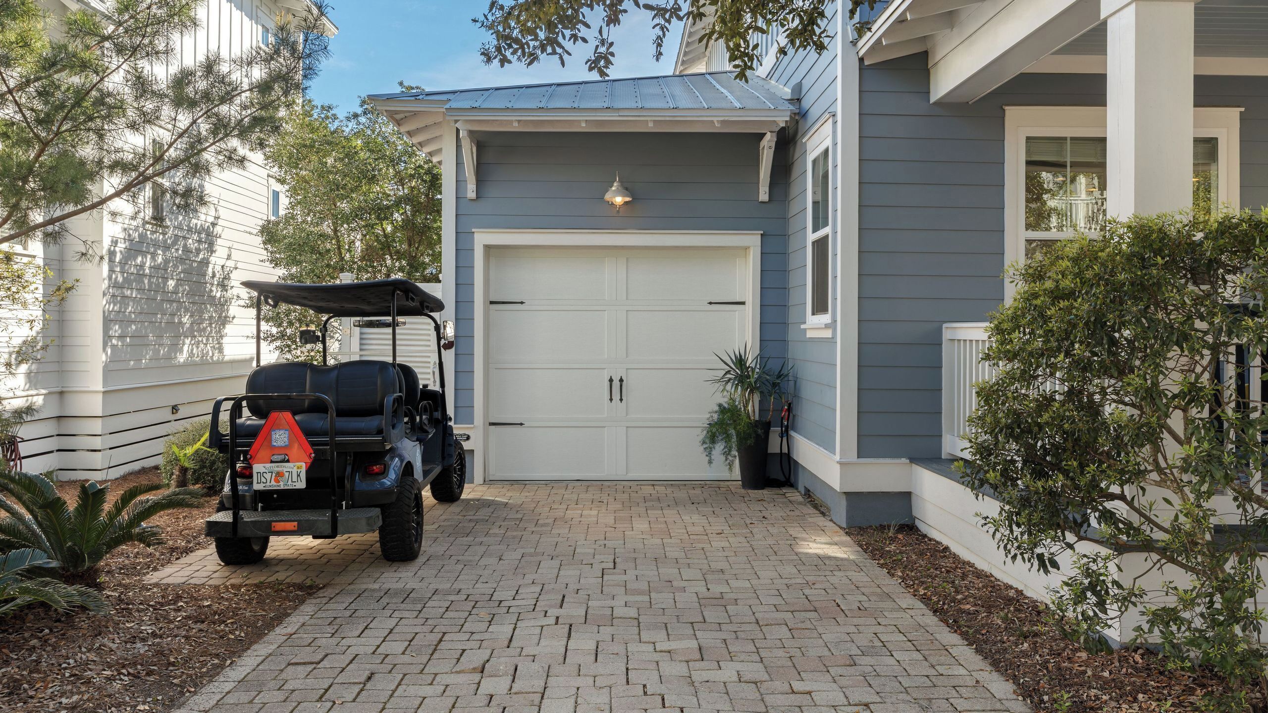 A residential garage with a golf cart parked in front, a driveway leading to the garage, and a house with a grey exterior and white trim.