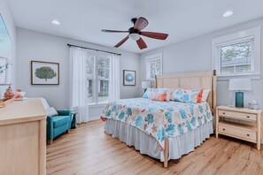 Une chambre à coucher comprenant un lit, un bureau, une chaise, une table de chevet et un ventilateur de plafond.