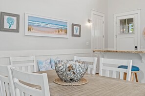 Un coin repas avec une table en bois, des chaises blanches, un centre de table décoratif en forme de bol en métal et des œuvres d’art encadrées accrochées au mur.