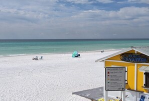 A beach with a sign indicating beach warning flags and a beach concessionaire.