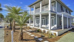 A two-story house with a covered porch, outdoor seating, and a landscaped garden. - All Decked Out by Avantstay Pool & Private Beach Access, Bikes Provided (Panama City Beach)