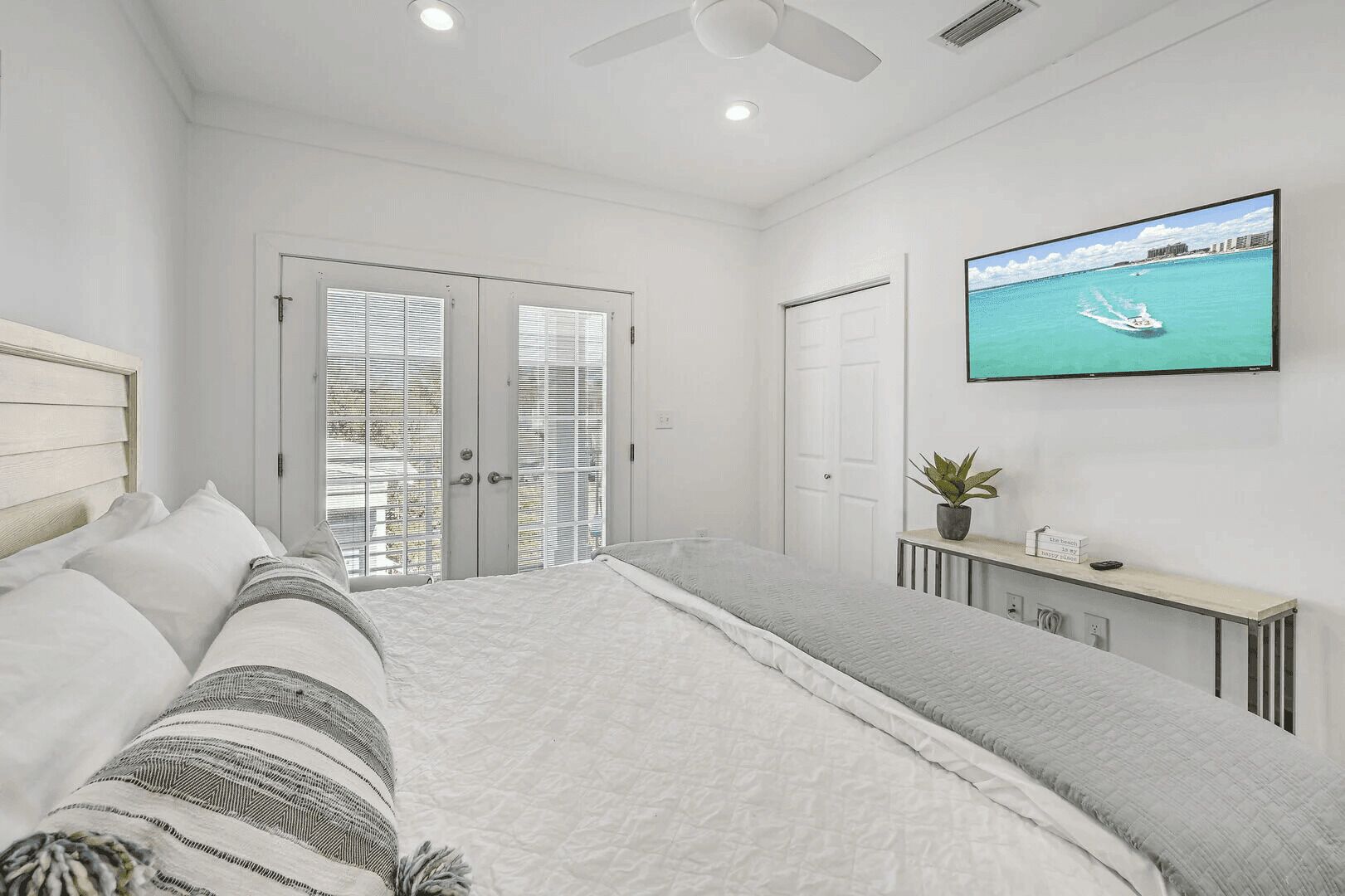 Un dormitorio con una cama grande, un televisor en la pared y una planta sobre una mesita de noche.
