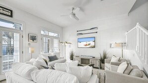 A spacious living room with white furniture, a ceiling fan, a TV, and a beach-themed decor. - All Decked Out by Avantstay Pool & Private Beach Access, Bikes Provided (Panama City Beach)