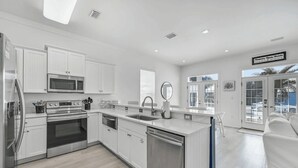A modern kitchen with white cabinetry, stainless steel appliances, and a large island with a sink. - All Decked Out by Avantstay Pool & Private Beach Access, Bikes Provided (Panama City Beach)