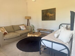 A room with a sofa, a small wooden table, a metal bed frame, and a painting on the wall.
