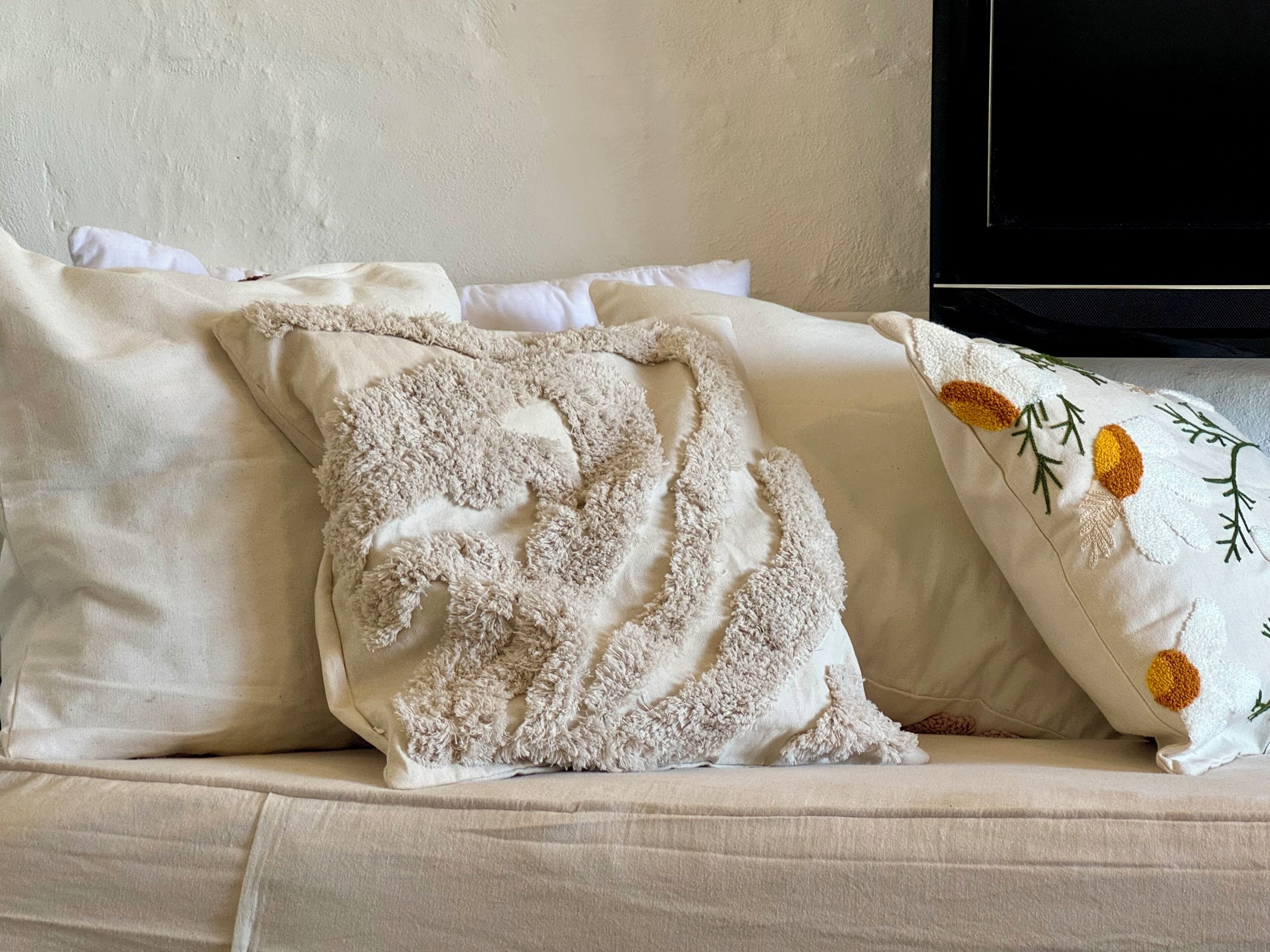 Un canapé beige agrémenté de trois coussins, dont l’un est moelleux et l’autre présente un motif floral.