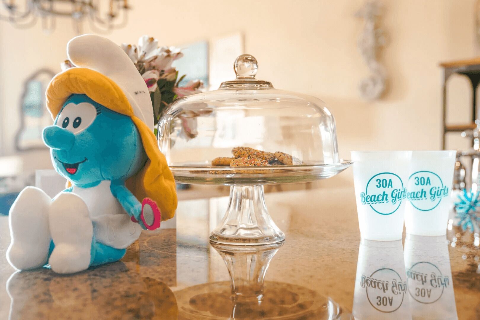 A plush toy, a glass cake stand with a lid, and a branded mug on a countertop.