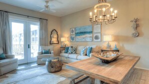 A spacious living room with a large wooden dining table, a glass coffee table, and a sofa set. - Smurf Mountain by Avantstay Private Beach + Pool Redfish Village (Santa Rosa Beach)