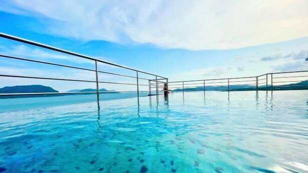 A clear view of an infinity pool with a metal railing, surrounded by calm water and distant mountains. - The Cube Langkawi (Langkawi)