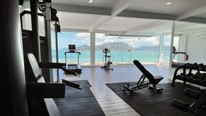 A gym with cardio equipment, weight machines, and dumbbells. It has large windows with a view of the sea and mountains. - The Cube Langkawi (Langkawi)