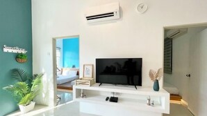 A modern living room with a flat-screen TV on a white entertainment unit, a green accent wall, and a door leading to another room. - The Cube Langkawi (Langkawi)