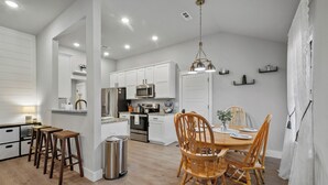 Una cocina moderna con armarios blancos, una zona de comedor con sillas de madera y un cubo de basura pequeño.