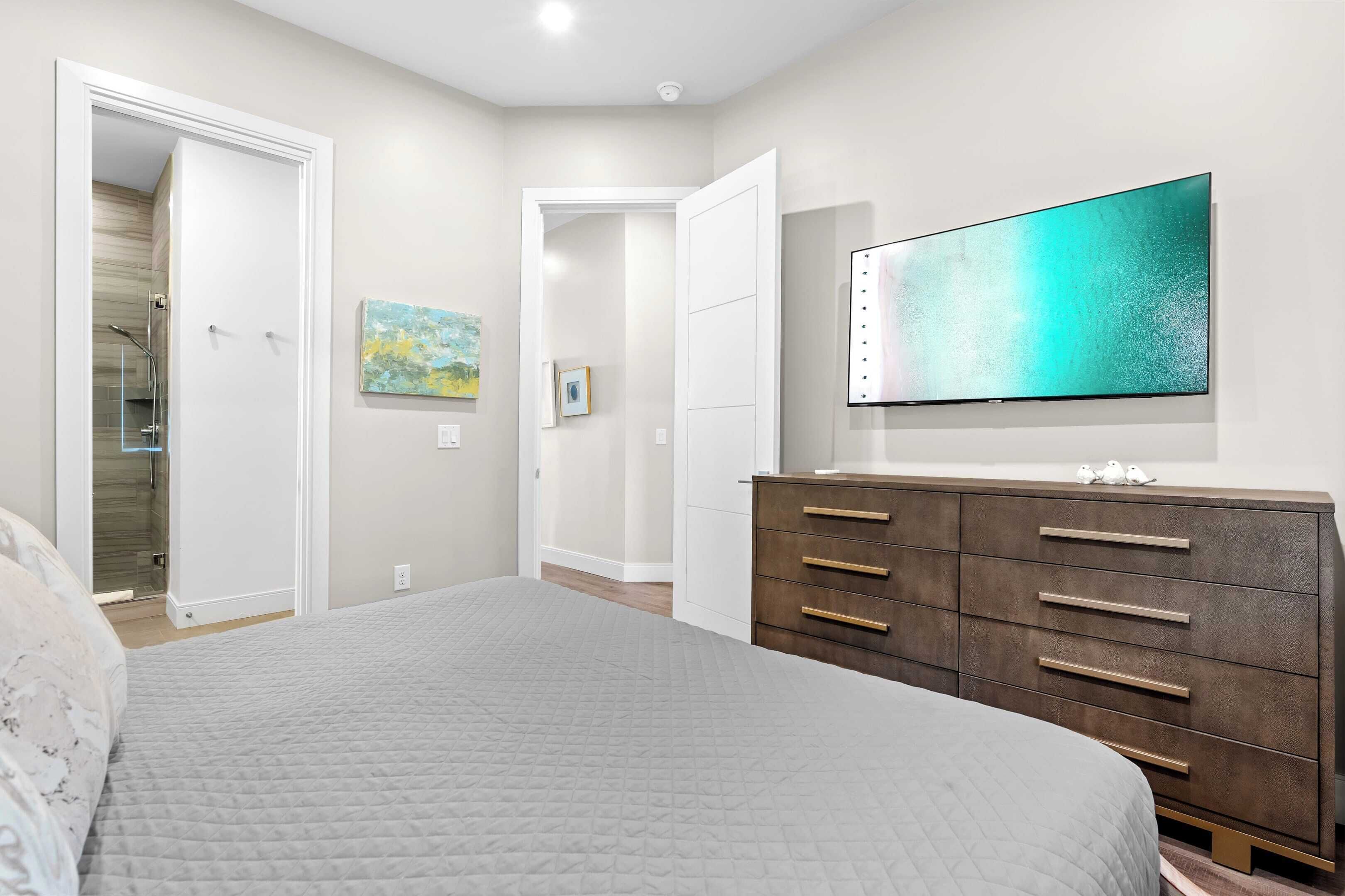 A bedroom with a bed, a dresser, a television, and a door leading to a bathroom.