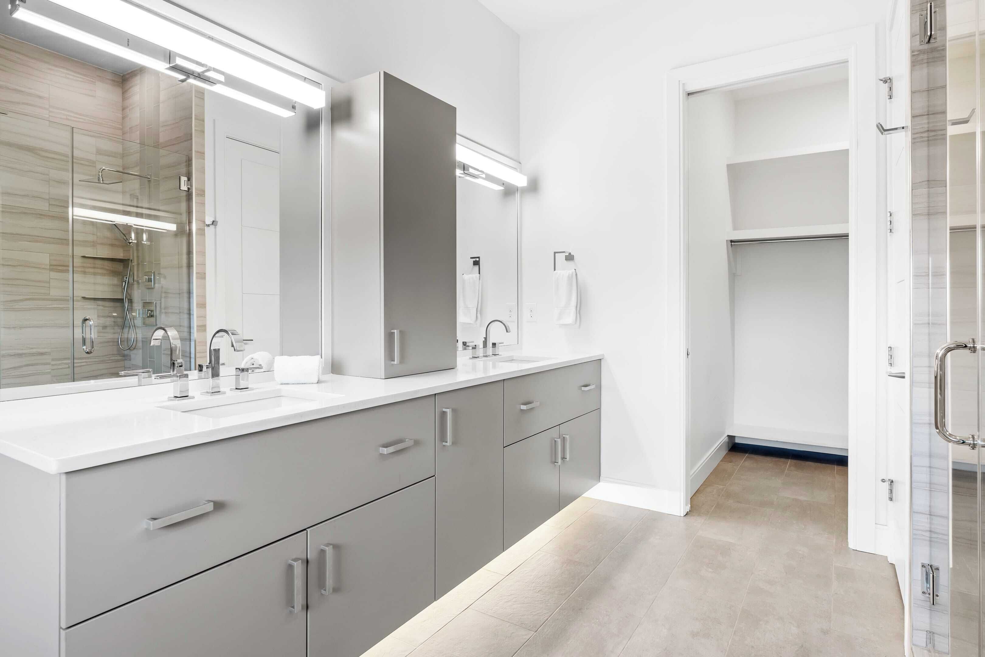 A modern bathroom with a large mirror, dual sinks, and a walk-in shower.
