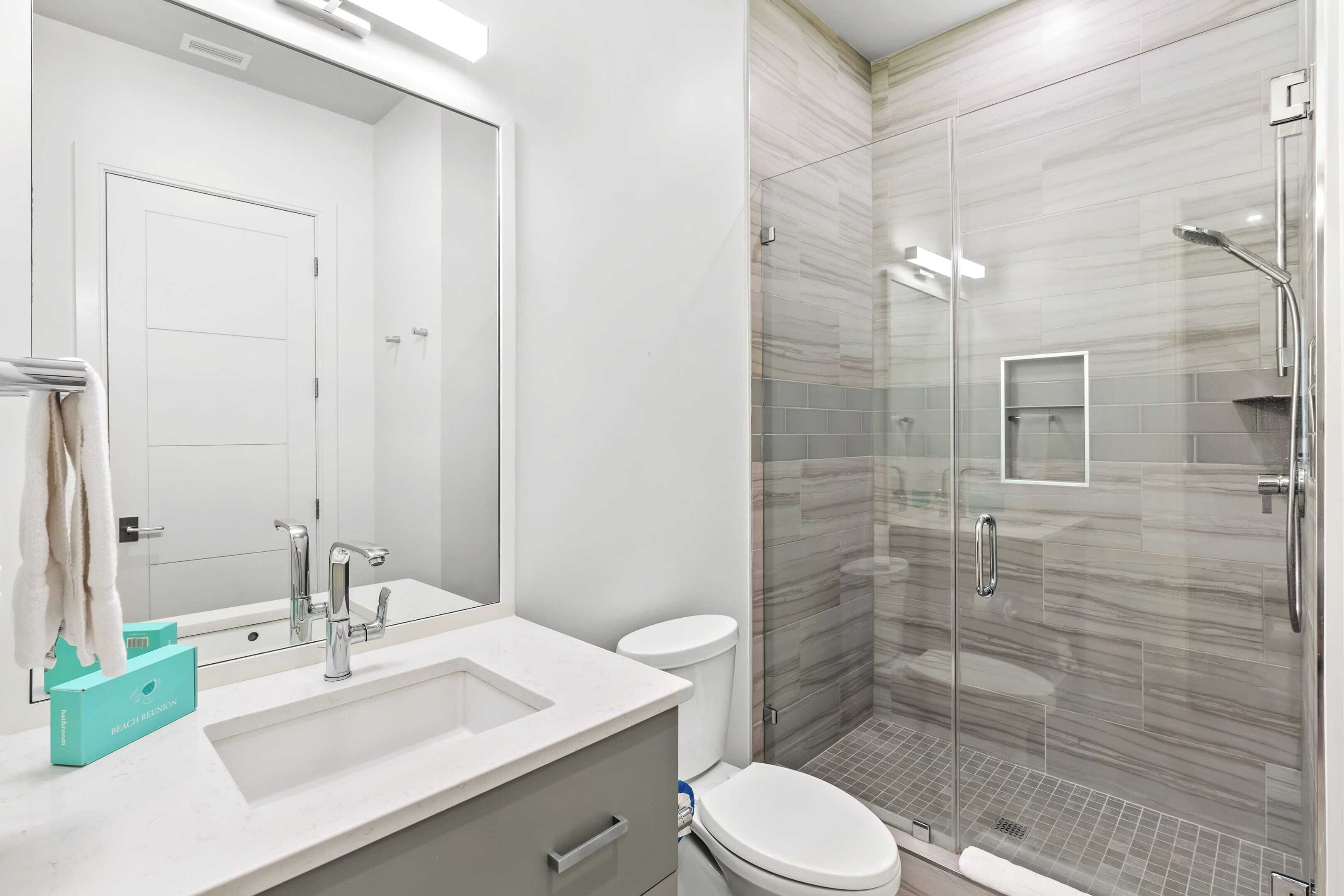 Une salle de bain moderne avec une douche à parois de verre, un lavabo blanc et un grand miroir.