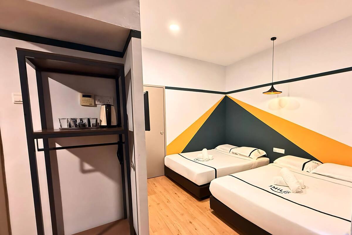 A hotel room with two beds, a kitchenette, and a wooden floor.