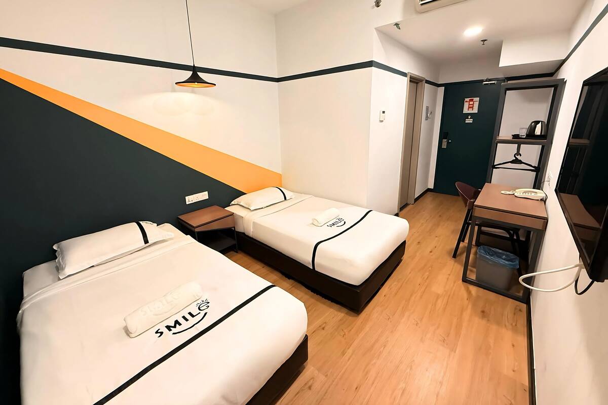 A hotel room with two beds, a desk, a chair, an air conditioner, and a small table with a telephone.