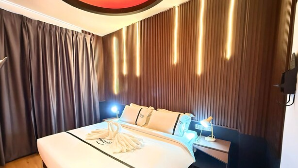 A modern hotel room with a large bed, a bedside table with a lamp, and a wall with vertical blinds. - Seeds Hotel Puchong Koi (Puchong)