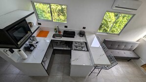 A modern kitchen with a gas stove, microwave, and sink. There are two windows providing natural light and a view of greenery outside.