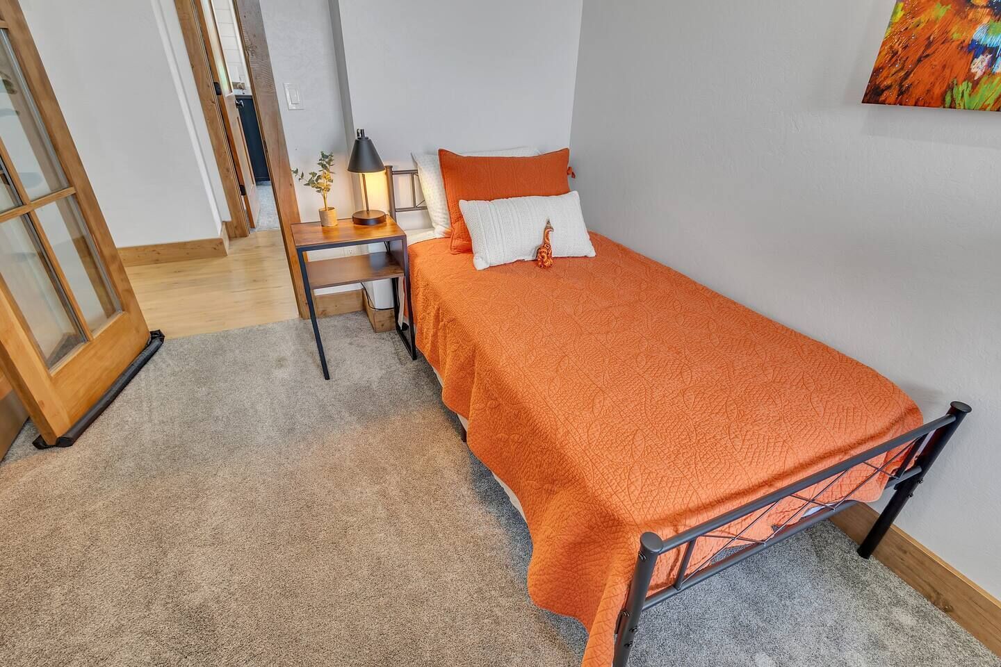 A bedroom with a bed, a desk, a chair, a lamp, and a door.